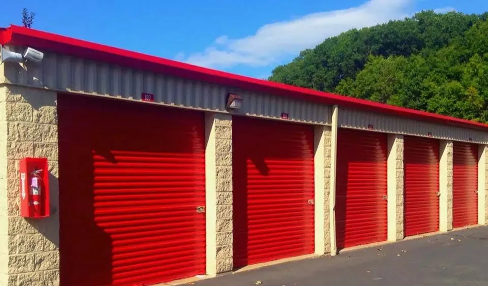 Row of red self-storage unit doors with security camera and fire safety equipment